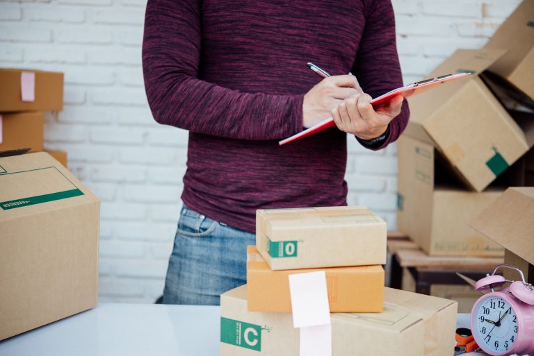 Handsome Young man working with papers among parcels at table in delivery department. online concept.